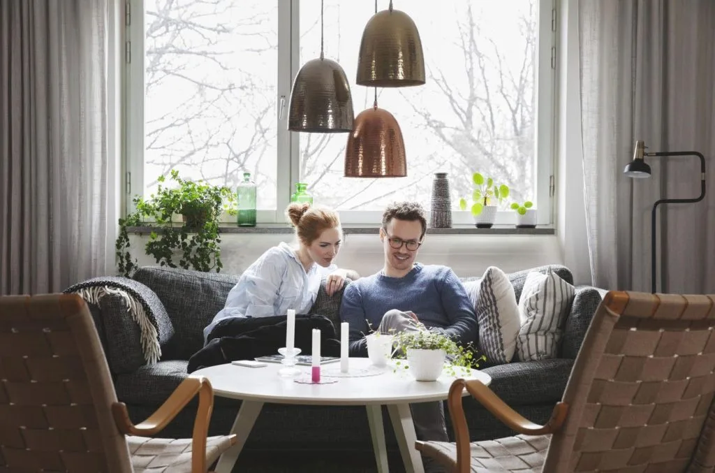 Nainen ja mies istuvat sohvalla ja katsovat miehen kädessä olevan puhelimen näyttöä